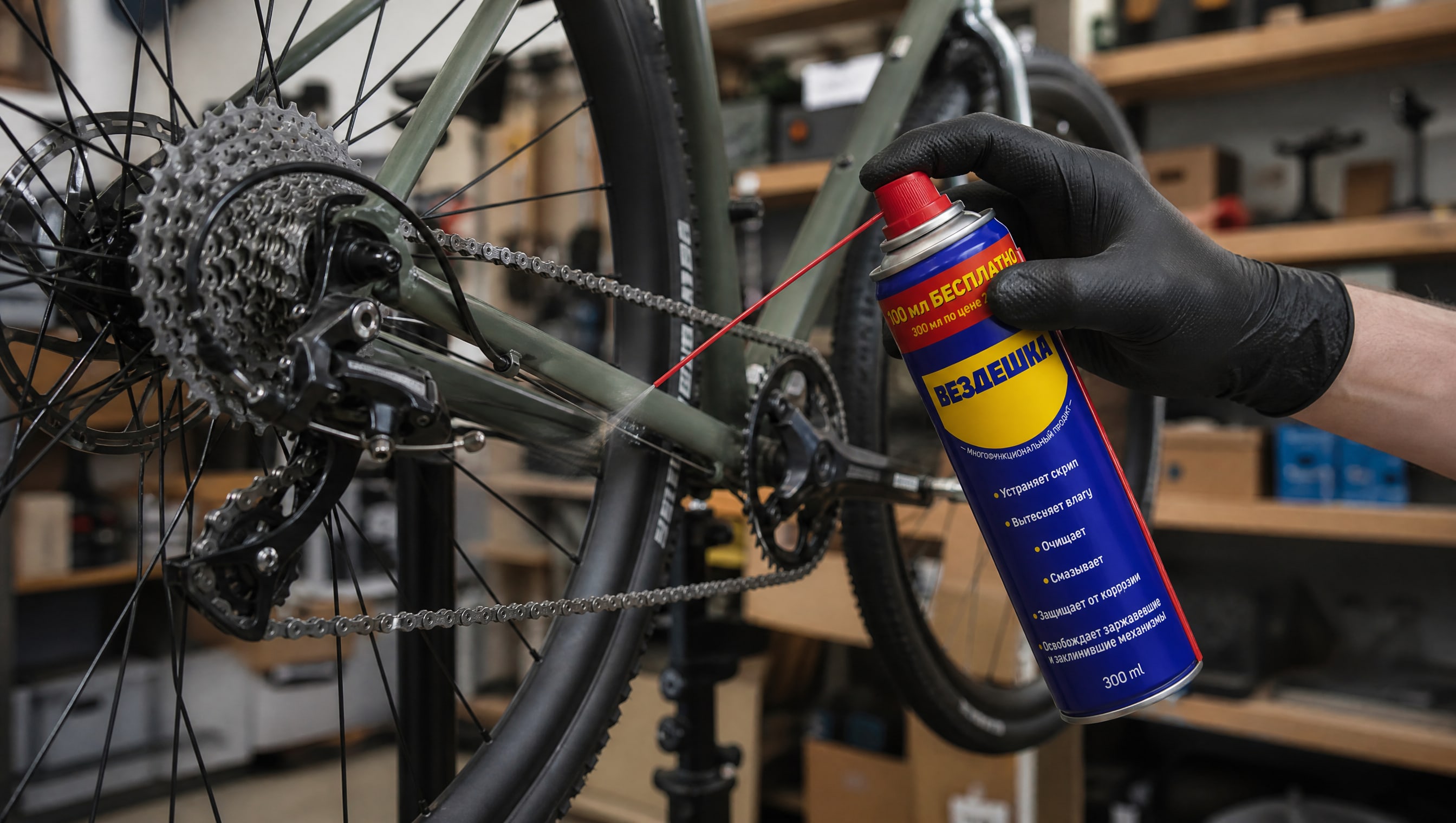 Рука в перчатке наносит универсальную смазку WD40 на велосипедную цепь.