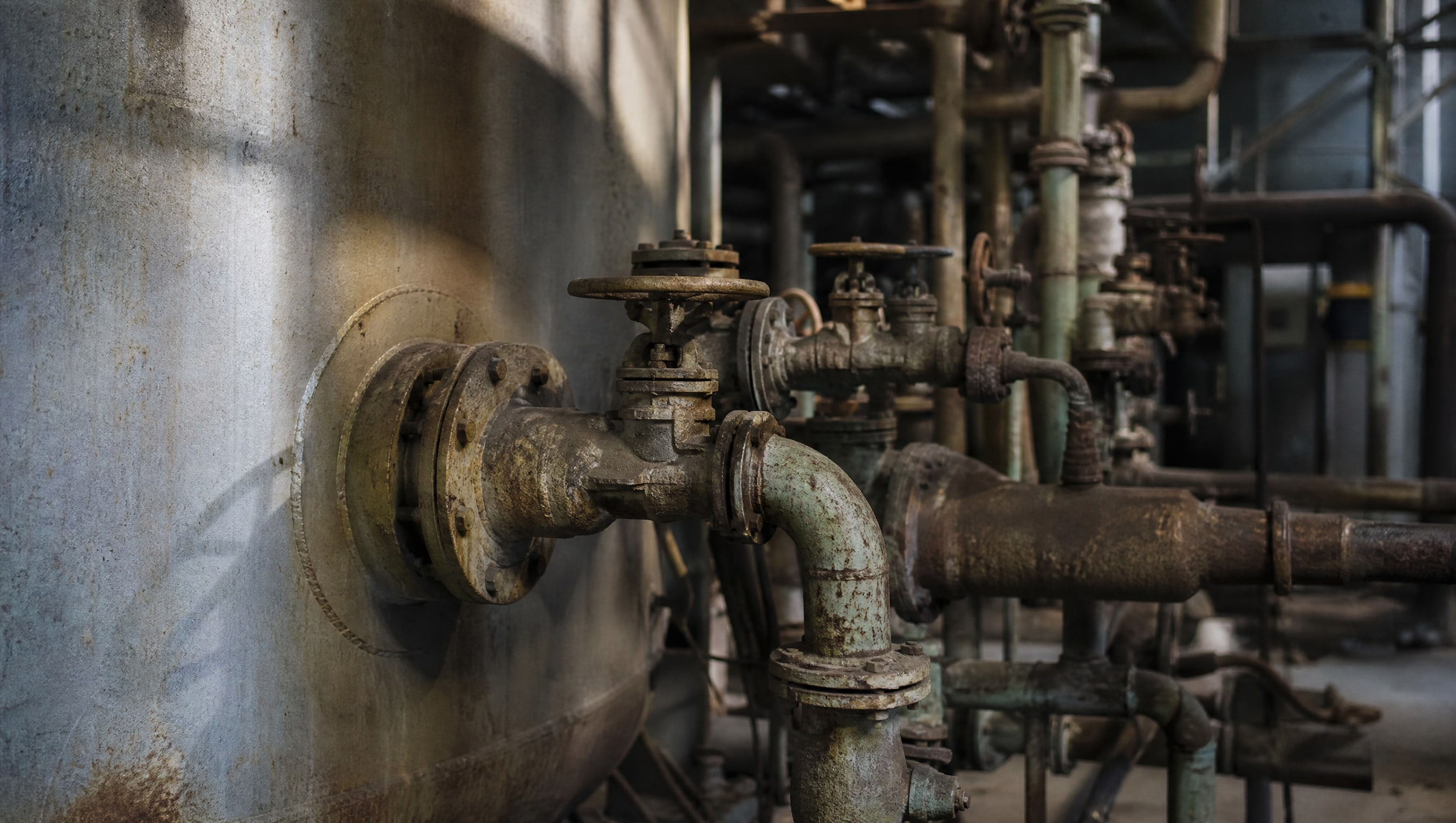 Механизм внутренней коррозии металлических деталей. Вид на старый трубопровод с клапанами, присоединенный к резервуару, где заметна коррозия внутренних поверхностей. Механизм внутренней коррозии металлических деталей. Вид на старый трубопровод с клапанами, присоединенный к резервуару, где заметна коррозия внутренних поверхностей.