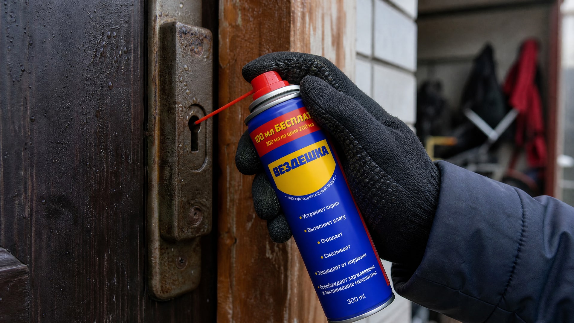 Рука в перчатке наносит универсальную смазку WD-40 на замок.