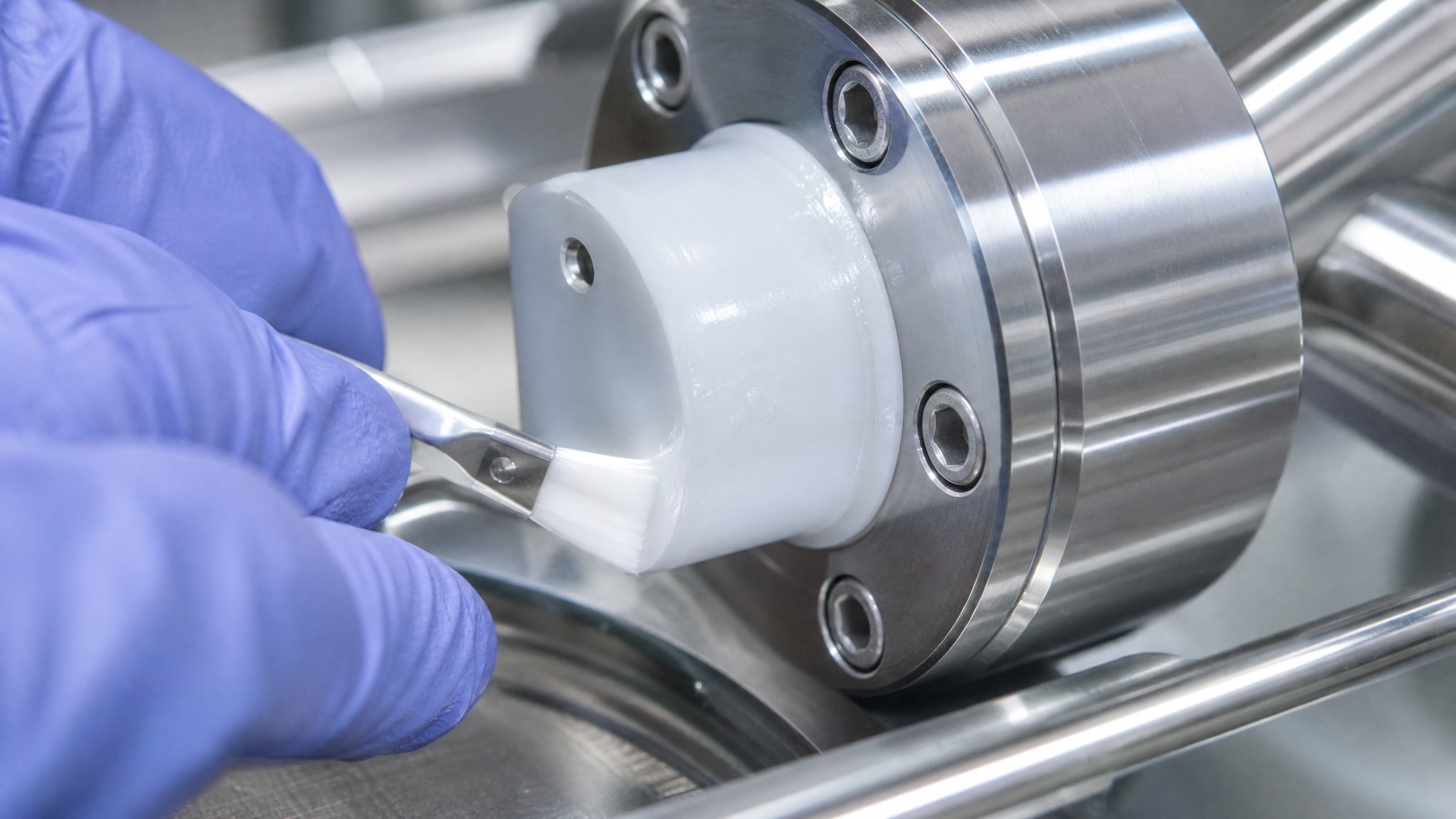 Гладкая PTFE деталь, частично покрытая смазкой, на фоне полированной нержавеющей стали пищевого насоса, демонстрирует низкий коэффициент трения материалов.